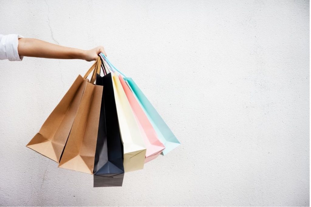 an arm holding out different coloured bags to signify shopping. How to save money by using Tesco Club Card Points for travel, holidays and day trips