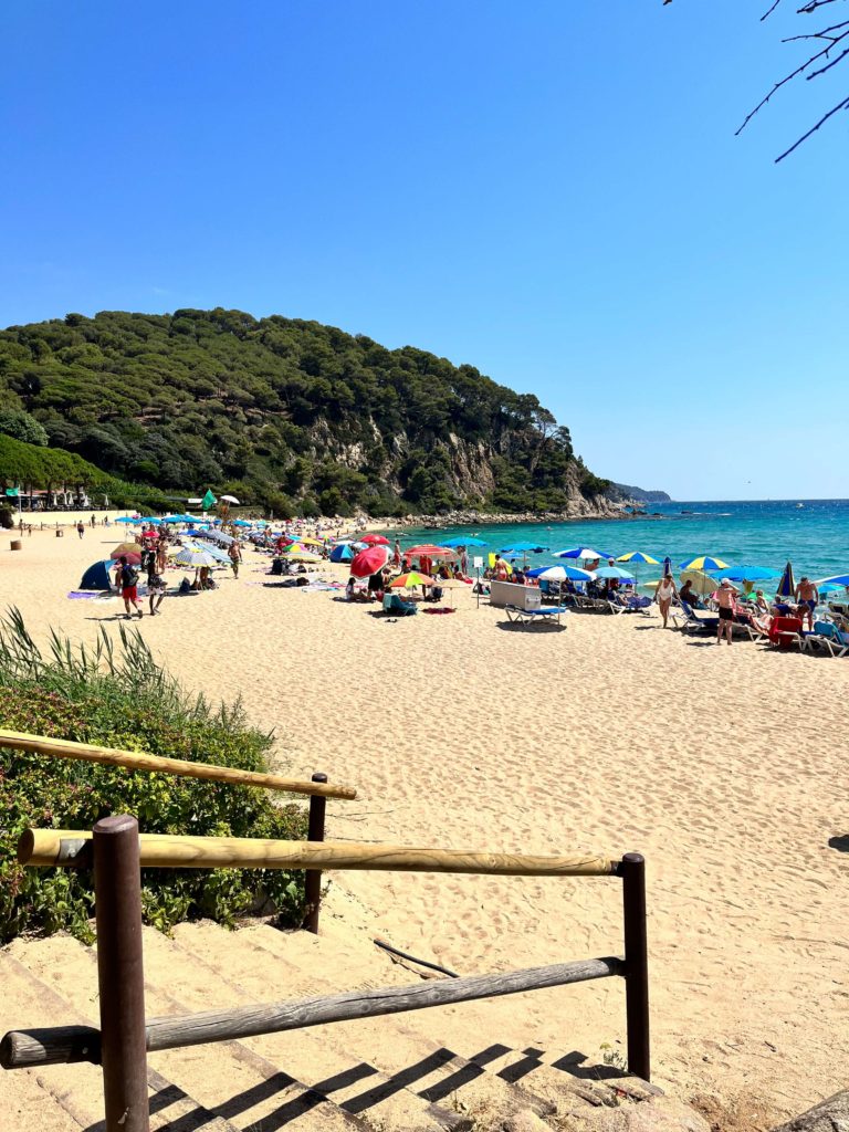 Platja De Santa Cristina. Sandy beach with umbrellas and green blue sea in distance. 